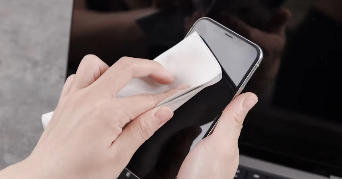 Hand wiping an iPhone with a soft microfiber cloth.