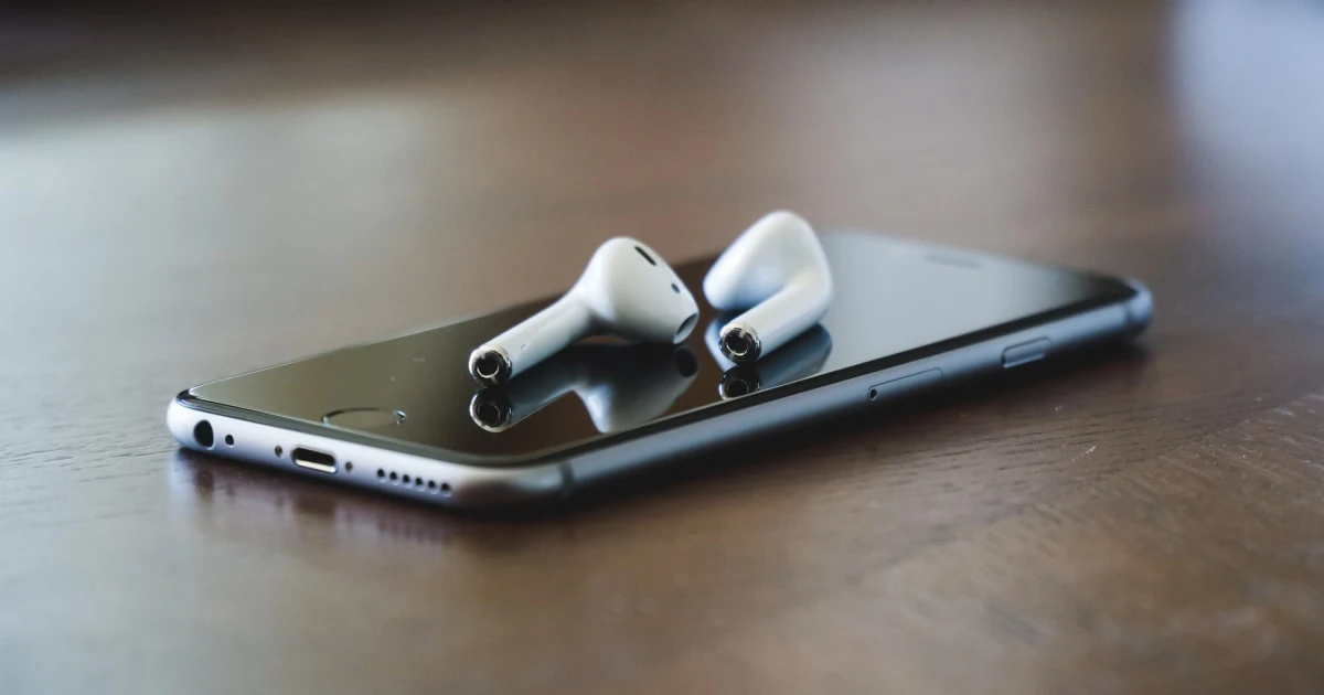AirPods resting on an iPhone on a wooden table.