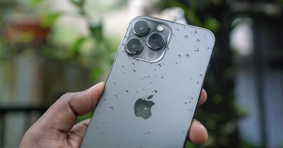 Hand holding an iPhone covered in water droplets.