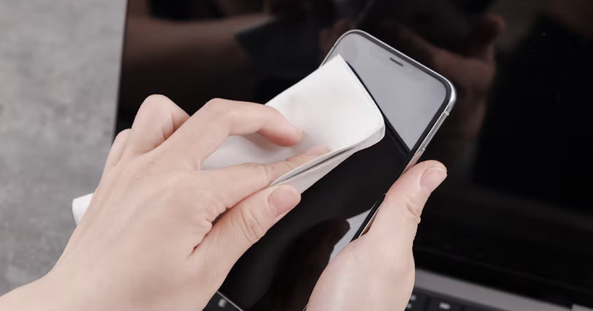 Hand wiping an iPhone with a soft microfiber cloth.