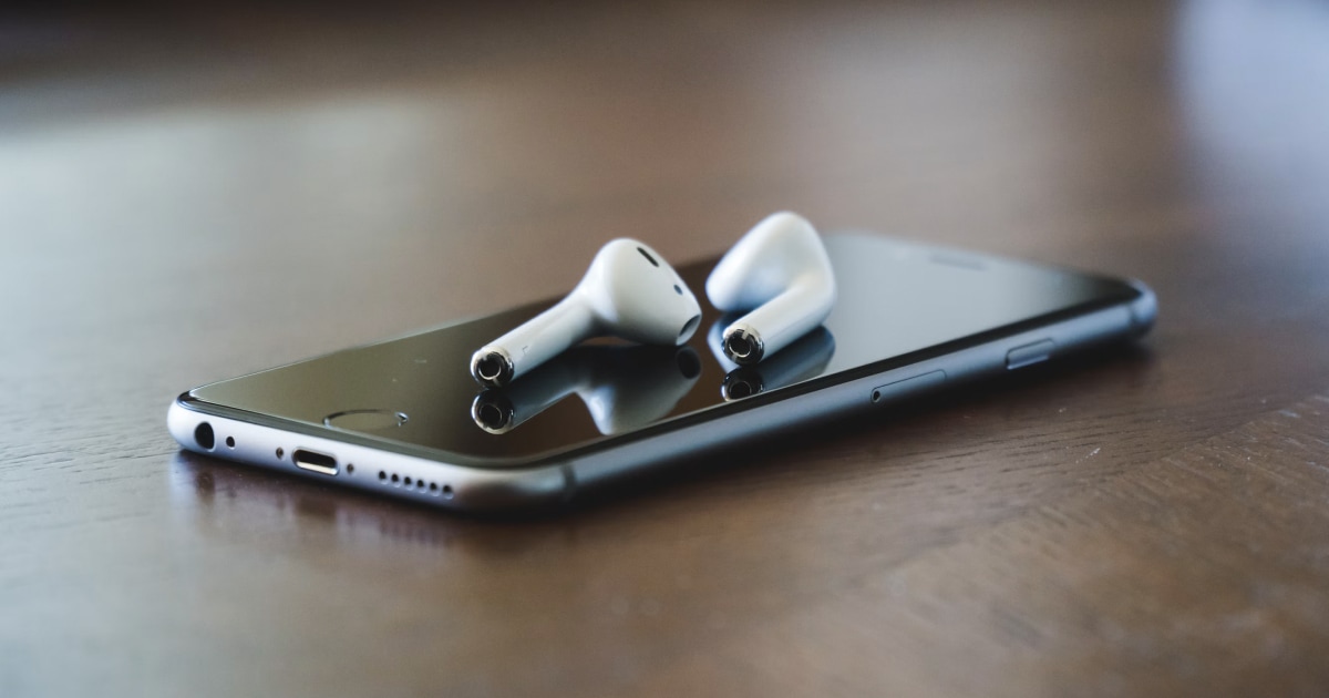 AirPods resting on an iPhone on a wooden table.